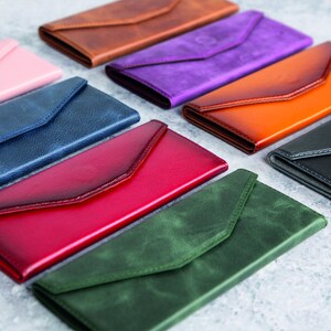 Pode incluir: Uma cole&ccedil;&atilde;o de carteiras de couro em formato de envelope em v&aacute;rias cores, incluindo rosa, castanho, roxo, laranja, preto, vermelho, azul e verde. Cada carteira apresenta um fecho de aba e um design elegante e minimalista.