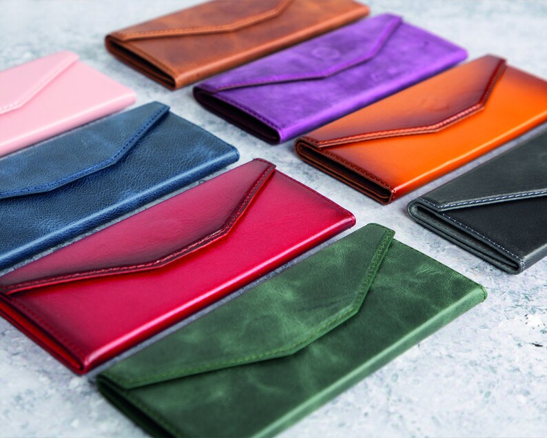 Pode incluir: Uma cole&ccedil;&atilde;o de carteiras de couro em formato de envelope em v&aacute;rias cores, incluindo rosa, castanho, roxo, laranja, preto, vermelho, azul e verde. Cada carteira apresenta um fecho de aba e um design elegante e minimalista.