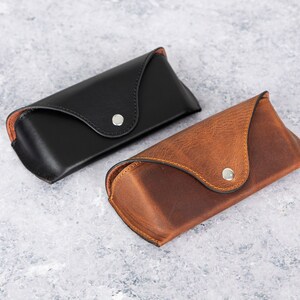 May include: Two leather eyeglass cases, one black and one brown. Both cases have a flap closure with a silver button.