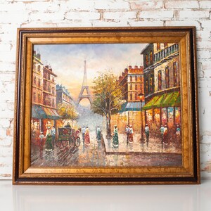 May include: Oil painting of a Parisian street scene with the Eiffel Tower in the background. The artwork features a horse-drawn carriage, pedestrians, and buildings with awnings. The painting is framed in a gold-colored wooden frame.