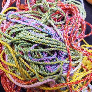 May include: A close-up of a tangled collection of colourful yarn. The yarn is in shades of red, yellow, green, blue, and pink. The twisted and braided yarn creates a textured appearance. Suitable for various craft projects.