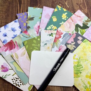 May include: A stack of colorful floral patterned note cards with a black Sharpie pen on top of a white card.