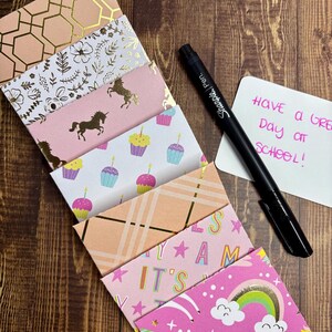 May include: A stack of pink and gold patterned gift cards with a black Sharpie pen and a white note that says "Have a great day at school!"