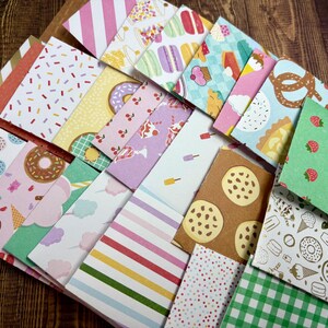 May include: A collection of colorful patterned paper squares with various designs, including donuts, strawberries, ice cream cones, and cookies. The papers are arranged in a random pattern on a wooden surface.