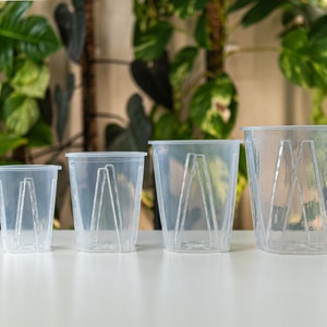 May include: Four clear plastic plant pots of varying sizes. The pots have a geometric design with a series of vertical lines.
