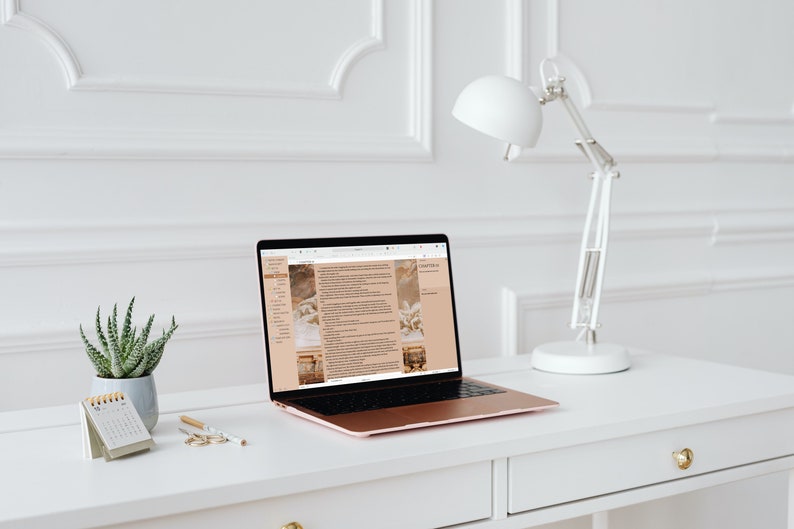 Puede incluir: Un espacio de trabajo moderno con un port&aacute;til de oro rosa que muestra una p&aacute;gina web, un calendario peque&ntilde;o, una planta suculenta en una maceta gris y una l&aacute;mpara de escritorio blanca. El escritorio es blanco con tiradores dorados, contra una pared blanca.