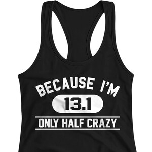 May include: Black racerback tank top with white text that reads "BECAUSE I'M 13.1 ONLY HALF CRAZY". The text is centered on the front of the tank top. The tank top has a scoop neck and a racerback design.