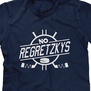 May include: A navy blue t-shirt with a white graphic of hockey sticks and a puck. The graphic says "No Regretzkys".