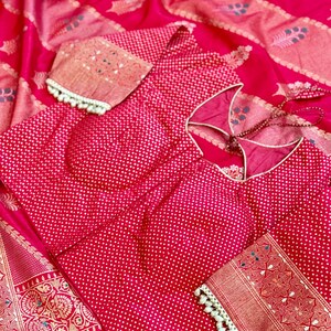May include: A red and gold patterned silk saree with a red polka dot blouse. The blouse has a low back and white pearl trim on the sleeves.