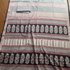 May include: A patterned textile featuring alternating bands of color and design. The top section has horizontal stripes in pink and gray. Below are bands of black floral patterns, red and white paisley, and geometric patterns. The edges are black.