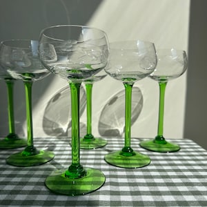 May include: Six clear wine glasses with etched floral patterns. The stems and bases are bright green. The glasses are displayed on a grey and white checkered tablecloth.