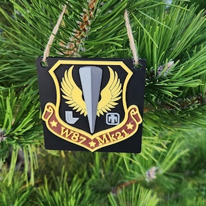 May include: Black and yellow Christmas ornament with a winged emblem and the text "W87 MK21".