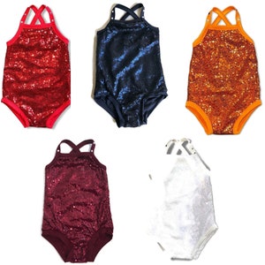 May include: Five sequined baby bodysuits in red, navy blue, orange, burgundy, and white. Each has a halter-style top with crisscross straps and contrasting trim around the legs and neckline. The bodysuits are designed for infants.