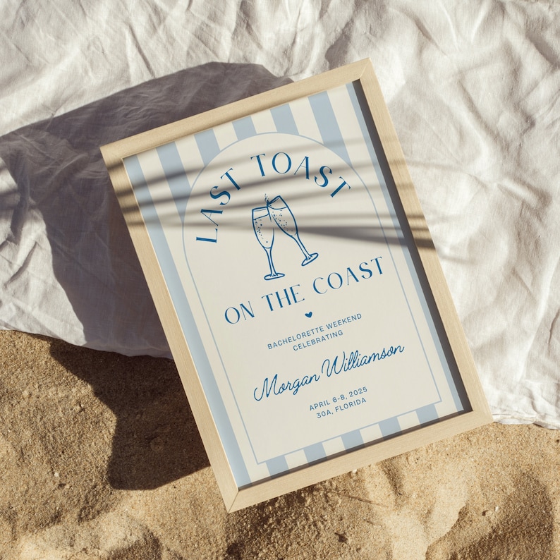 May include: A light blue and white striped sign with the text "Last Toast on the Coast" in blue lettering. The sign also includes a graphic of two champagne glasses clinking, a heart, and the text "Bachelorette Weekend Celebrating Morgan Williamson April 6-8, 2025 30A, Florida".