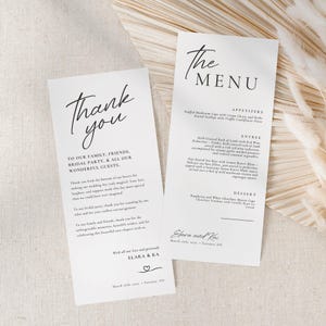May include: Two white wedding stationery cards with black text. One says "Thank you" and the other says "The MENU". The cards include the names "Elara & Kai" and the wedding date. The cards are for a wedding.