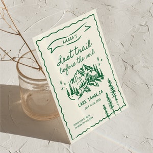 May include: A green and white invitation card with a mountain scene and a cabin. The text reads "Kierra's Last Trail Before The Veil" and "Lake Tahoe, CA July 11-13, 2025".