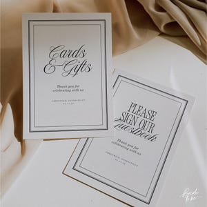 May include: Two white rectangular signs with black text and borders. One sign reads "Cards & Gifts" and the other says "Please Sign Our Guestbook." Both signs include the text "Thank you for celebrating with us."