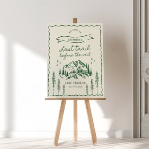 Op de afbeelding: Een groen en wit bord met de tekst "WELCOME TO SAVANNAH'S Last trail before the veil LAKE TAHOE,CA JULY 11-13, 2025" en een tekening van een hut in de bergen.