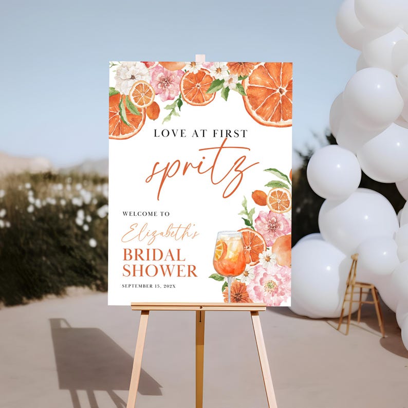 May include: A white bridal shower welcome sign with orange slices, flowers, and a glass of spritz. The text reads "Love at First Spritz, Welcome to Elizabeth's Bridal Shower, September 15, 202X".