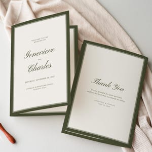 Può includere: Biglietti d'invito di nozze con interno bianco e bordo verde scuro. Le carte presentano i nomi "Genevieve e Charles" e la data "26 novembre 2027". Una carta recita "Grazie".