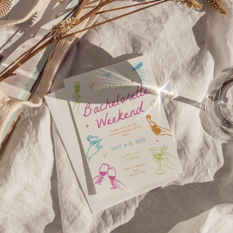 Op de afbeelding: Een witte kaart met roze, blauwe en groene illustraties van cocktails en champagne glazen. De tekst op de kaart luidt "Stefanie's Bachelorette Weekend" en bevat de datum "Sept 6-8, 2025" en de locatie "Siesta Key, Florida".