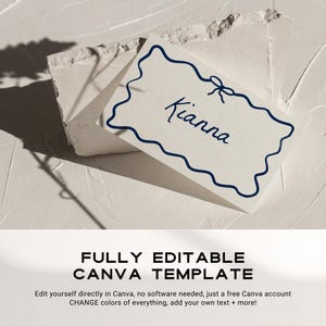 May include: A white card with a blue border and a blue bow at the top. The text "Kianna" is written in cursive on the card. The card is sitting on a white textured surface.
