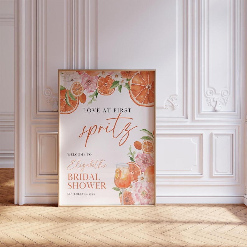 May include: A bridal shower sign with orange slices and flowers. The text reads "Love at First Spritz, Welcome to Elizabeth's Bridal Shower, September 15, 2023".