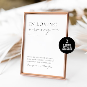 May include: A framed print with a rose gold border. The text reads "IN LOVING memory" above a line, followed by a quote about loved ones. A black circle with "2 DESIGN OPTIONS INCLUDED" is on the right.