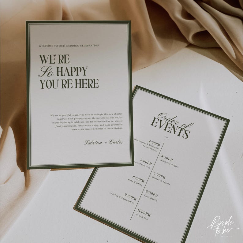 May include: Two wedding signs with green borders. One sign reads "WE'RE So HAPPY YOU'RE HERE" and the other lists the "Order of Events." The signs are on a white surface with a soft, neutral background.