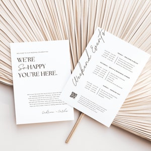 May include: A white wedding invitation with black text. The invitation reads "Welcome to our wedding celebration. We're so happy you're here." and includes the names Sabrina and Carlos. The invitation also includes a QR code and a schedule of events for the wedding weekend.