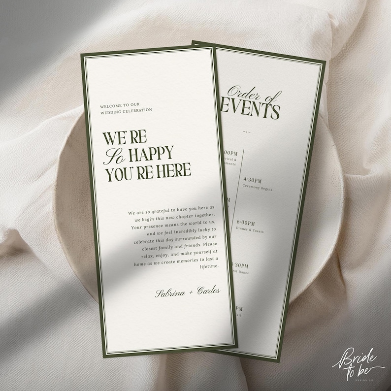 May include: Two wedding invitation cards with a green border and text. The first card reads "WE'RE So HAPPY YOU'RE HERE" and "WELCOME TO OUR WEDDING CELEBRATION". The second card reads "Order of EVENTS". The cards are on a white surface.