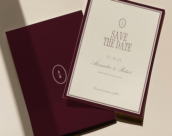May include: Burgundy "Save the Date" wedding invitation with a cream-colored insert. The text reads "Save the Date" above the date, names, and location. The invitation is in a burgundy envelope with the initials "A R" inside an oval.