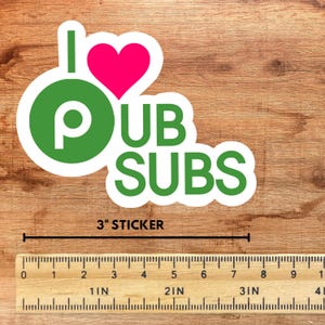 Puede incluir: Una pegatina blanca con el texto "I ♥ PUB SUBS" en verde y rosa. La pegatina mide 7,6 cm de largo e incluye una regla para medir.