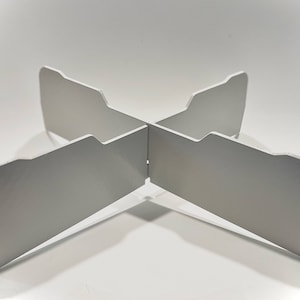 Op de afbeelding: Een witte metalen standaard met vier poten die een X-vorm vormen. De standaard is ontworpen om een ​​pan of andere kookapparatuur te houden.