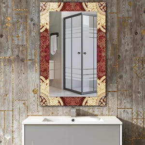 May include: Rectangular bathroom mirror with a decorative border. The border features a repeating pattern in burgundy, gold, and cream. The mirror reflects a shower enclosure and a white sink.