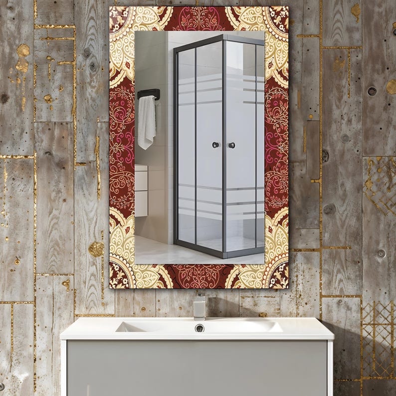 May include: Rectangular bathroom mirror with a decorative border. The border features a repeating pattern in burgundy, gold, and cream. The mirror reflects a shower enclosure and a white sink.