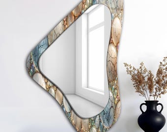 May include: An asymmetrical wall mirror with a decorative frame. The frame is adorned with a mosaic of colorful, oval-shaped stones in shades of blue, beige, and gold. The mirror is displayed on a dark wooden surface.