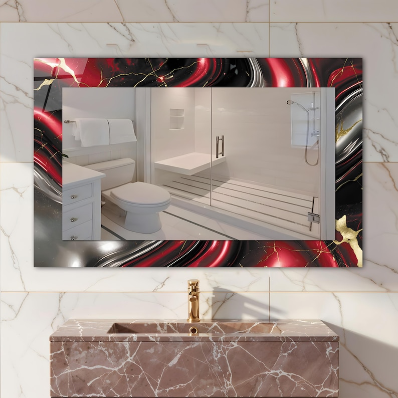 May include: Rectangular bathroom mirror with a decorative frame featuring a red, black, and silver abstract design with gold accents. The mirror reflects a modern bathroom with white fixtures and a glass shower.