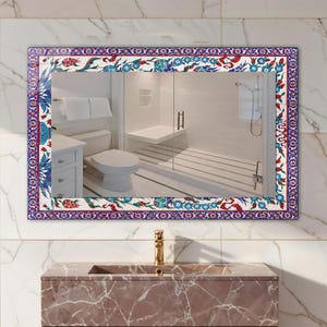 May include: Rectangular mirror with a decorative border featuring a floral pattern in red, blue, and white. The mirror reflects a bathroom scene with a toilet, shower, and vanity. The frame is a vibrant accent.