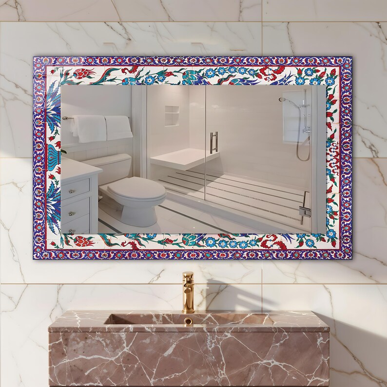May include: Rectangular mirror with a decorative border featuring a floral pattern in red, blue, and white. The mirror reflects a bathroom scene with a toilet, shower, and vanity. The frame is a vibrant accent.