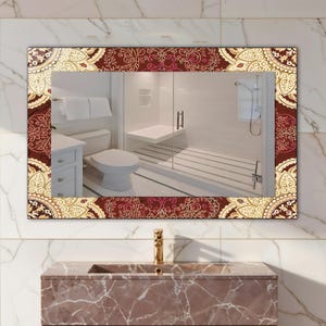 May include: Rectangular bathroom mirror with a decorative border featuring a burgundy, cream, and gold paisley design. The mirror reflects a bathroom with a toilet, shower, and vanity.