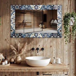 K&ouml;nnte beinhalten: Rechteckiger Spiegel mit einem dekorativen Rand mit blauen, wei&szlig;en und marinefarbenen Blumenmustern. Der Spiegel ist an einer Holzwand &uuml;ber einem wei&szlig;en, runden Waschbecken angebracht. Ein Holzregal enth&auml;lt Toilettenartikel und dekorative Vasen.