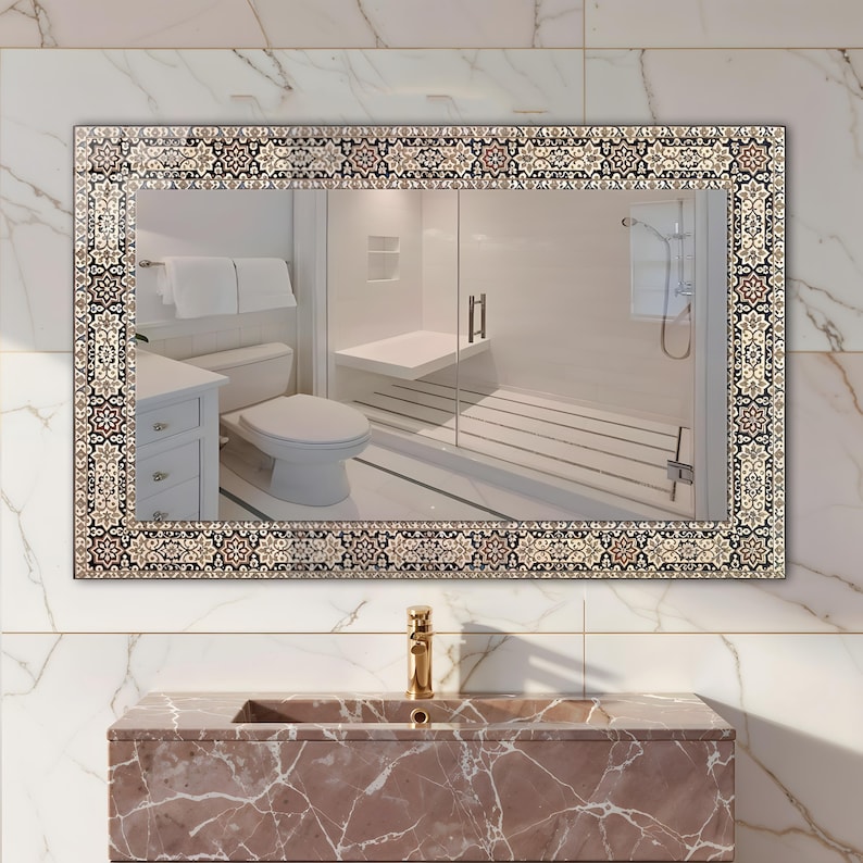 May include: Rectangular bathroom mirror with a decorative patterned border in shades of beige, brown, and black. The mirror reflects a bathroom with a white toilet, shower, and vanity. The vanity has a marble-like appearance.