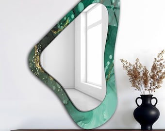 May include: An abstract-shaped wall mirror with a green and gold design. The mirror has a unique, irregular shape with a teal and gold pattern around the edges. The mirror is displayed on a dark brown table.