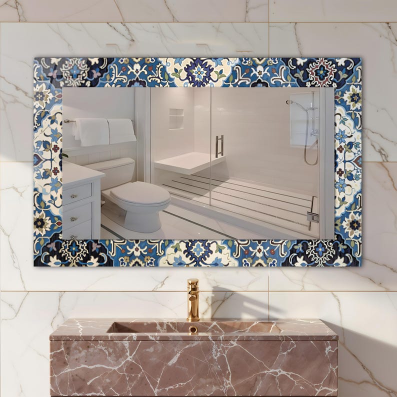 K&ouml;nnte beinhalten: Rechteckiger Badezimmerspiegel mit dekorativem Rand mit blauem, wei&szlig;en und beigen Blumenmuster. Der Spiegel spiegelt ein Badezimmerinterieur mit Toilette, Dusche und Waschbecken wider. Das Waschbecken ist aus rotbraunem Marmor.