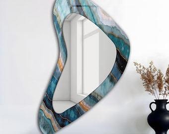 May include: An abstract-shaped wall mirror with a blue, teal, and gold marbled design. The mirror has a unique, organic shape and is mounted on a white wall. A dark brown shelf and a black vase with dried plants are in the foreground.