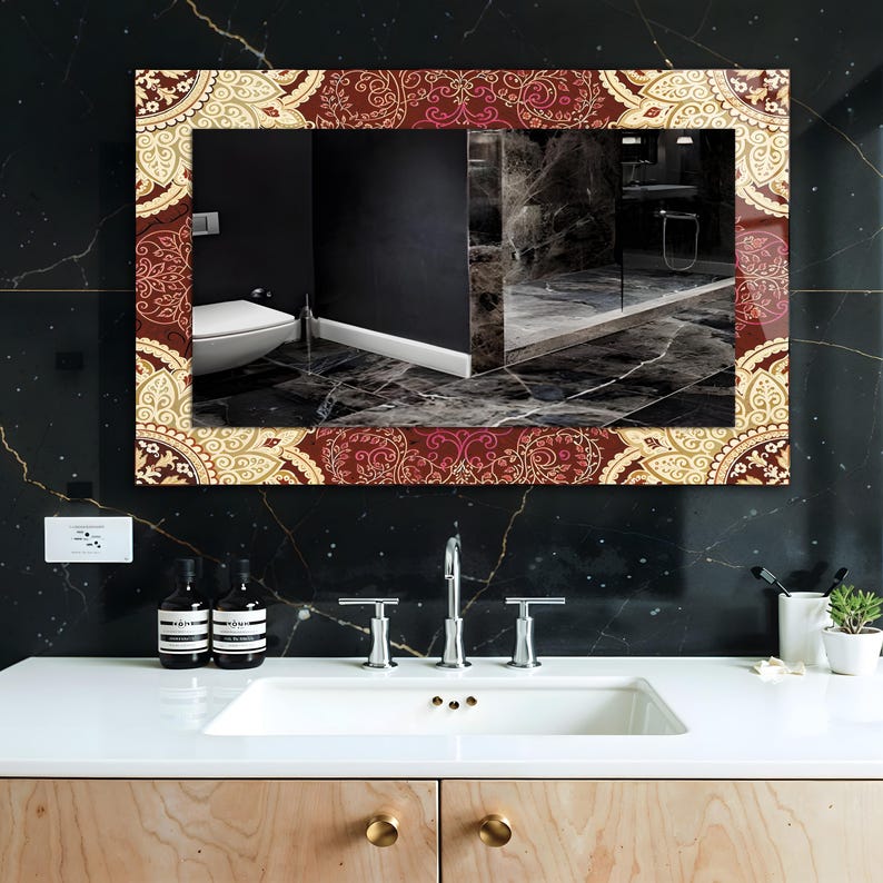 May include: Rectangular mirror with a decorative border featuring a burgundy and cream paisley pattern. The mirror is mounted on a black marble wall above a white sink with chrome fixtures. The bathroom setting is reflected in the mirror.