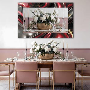 May include: A dining room scene featuring a wooden table set for a meal. A large gold bowl filled with white flowers is the centerpiece. Pink chairs with gold frames surround the table. A decorative abstract art piece with red, black, and gold accents hangs on the wall.