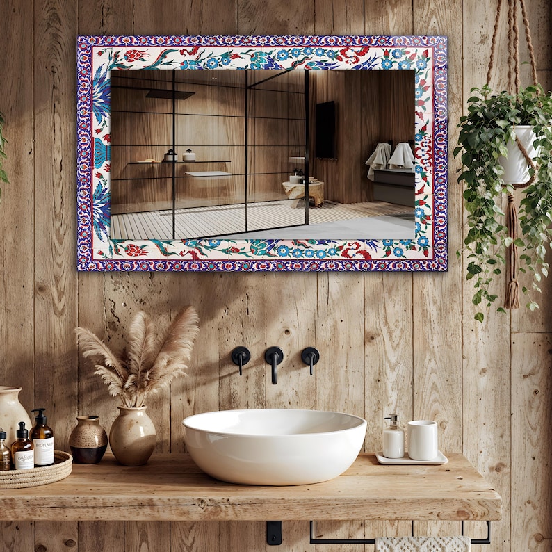 May include: Rectangular mirror with a decorative border featuring a floral pattern in blue, red, and green on a white background. The mirror is mounted on a wooden wall above a white sink, enhancing the bathroom's aesthetic.