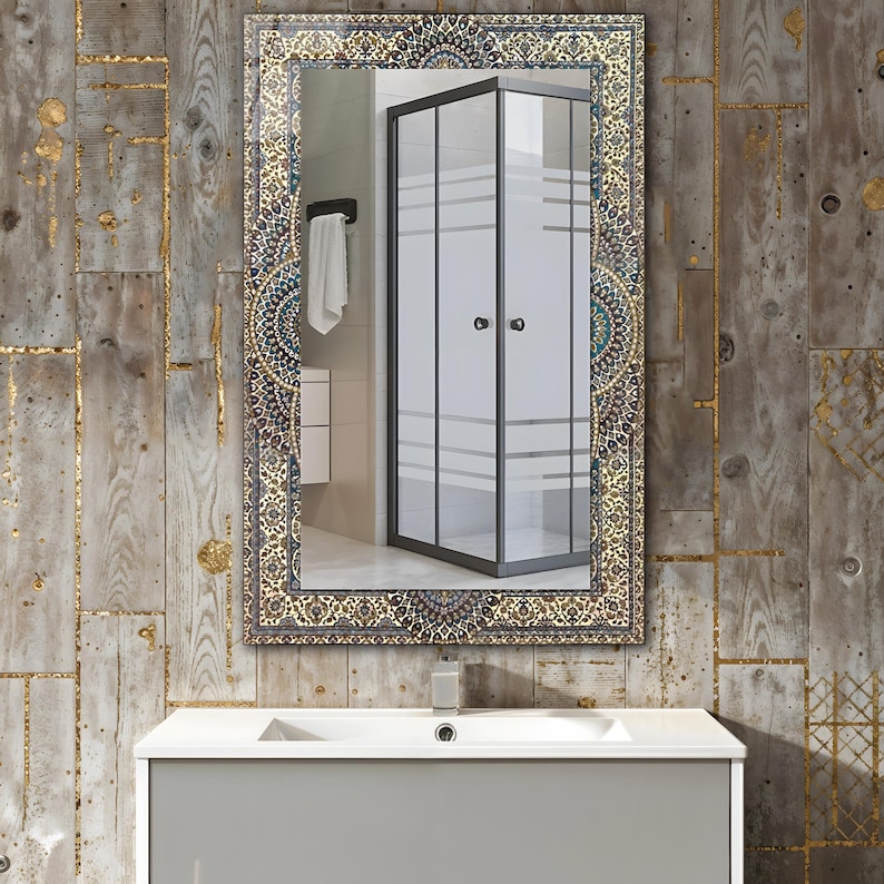 K&ouml;nnte beinhalten: Ein rechteckiger Spiegel mit einem verzierten, gemusterten Rahmen in Gold-, Blau- und Beiget&ouml;nen. Der Spiegel spiegelt eine moderne Duschkabine, ein wei&szlig;es Handtuch und einen grauen Waschtisch mit einem wei&szlig;en Waschbecken wider. Der Hintergrund ist eine Holzwand.